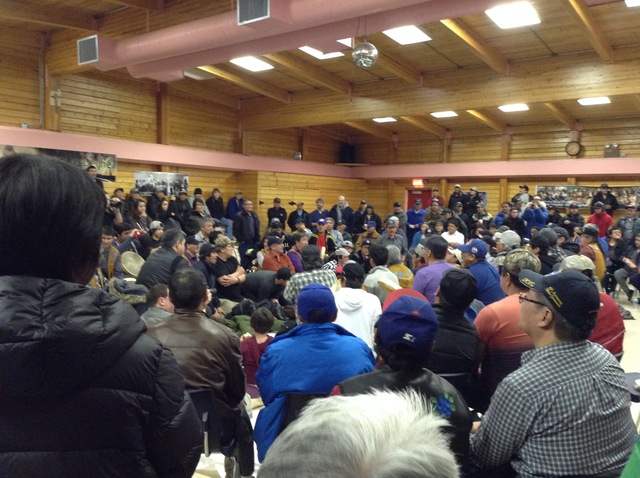 People seated in a circle in a wooden hall, with drummers and singers at the centre.