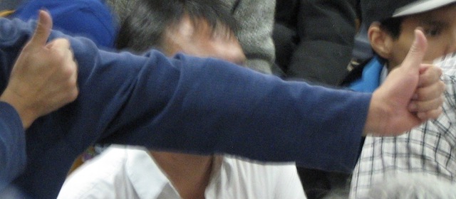 Group scene with two hands giving a thumbs-up gesture in the foreground.