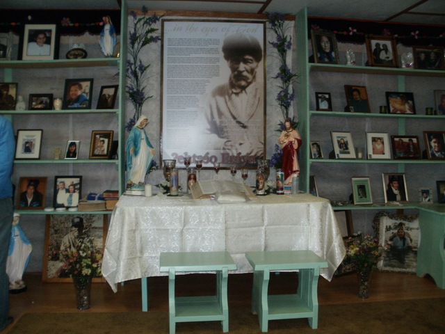 Altar dedicated to Ahya with a portrait, religious objects, candles, books, and surrounding photographs.