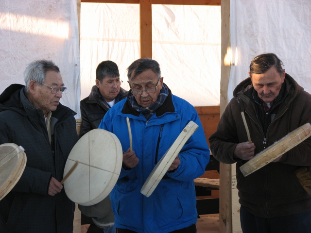 Charlie Neyelle, Alfred Taniton, and Leon Modeste wearing winter jackets and playing hand drums.