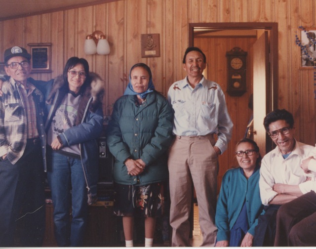 Six men and women standing and sitting together in a wood-paneled room.